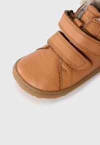 Zapato infantil de cuero color tostado con un acabado texturizado, que cuenta con dos correas ajustables de velcro y una suela de goma flexible.
