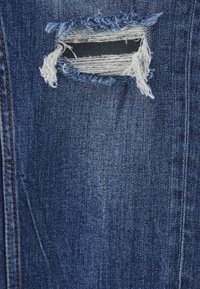 Tissu en denim bleu déchiré avec une déchirure horizontale montrant des fils blancs et un tissu noir en dessous.