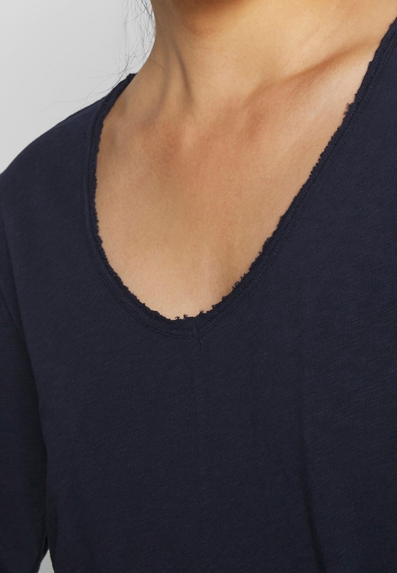 Navy blue top made from soft fabric with a deep V-neck design and raw edge details on the neckline. Short sleeves, casual fit.