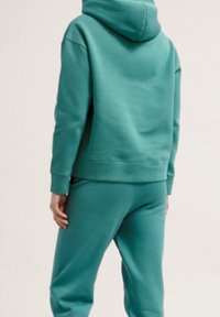 Sweat à capuche turquoise et pantalon assorti en tissu doux et texturé, avec une capuche de taille moyenne et des poignets côtelés pour le confort.