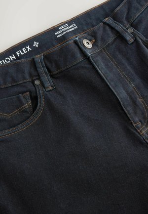 Mørk denim jeans med orange syninger, almindelig tapered fit, med lommer og metal knaplukning. Etiket ovenfor med plejeinstruktioner.