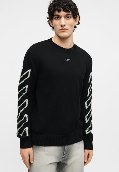Νεαρός με σγουρά μαλλιά που φοράει μαύρο πουλόβερ με λευκά ζιγκ-ζαγκ σχέδια στα μανίκια και μικρό κείμενο "OFF" στο στήθος.