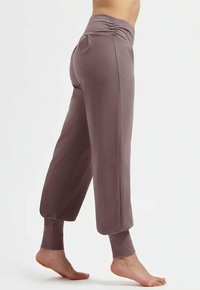 Lila, korta träningsbyxor med borstad textur, veckad midjedetalj och åtsittande muddar vid anklarna, designade för komfort och rörelsefrihet.