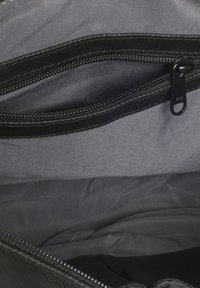 Interno di una borsa nera in tessuto con una superficie liscia e due scomparti con zip. La fodera è in materiale grigio scuro, caratterizzata da cuciture discrete.