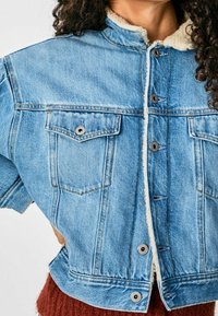 Ljusblå denimjacka med krage och knappstängning. Har två bröstfickor och en mjuk, vit, fluffig foder.