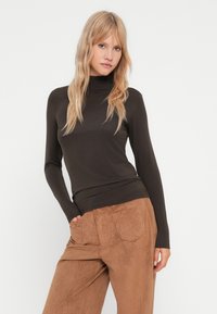 Brun langærmet turtle neck top lavet af blødt, strækbart stof, parret med lysebrune bukser i semilæder med bred benvidde og baglommer.