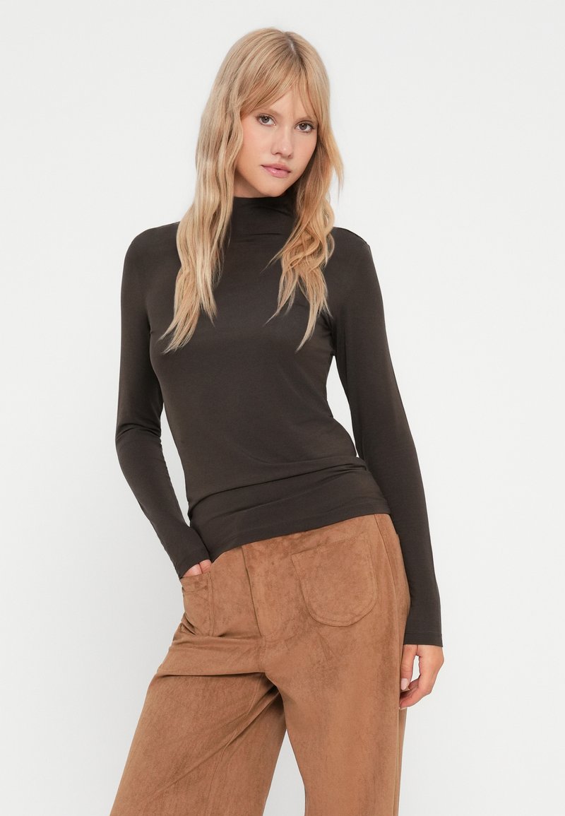 Brązowy sweter z długim rękawem i golfem, wykonany z miękkiej, elastycznej tkaniny, zestawiony z jasnobrązowymi spodniami o szerokich nogawkach przypominającymi zamsz, z tylnymi kieszeniami.