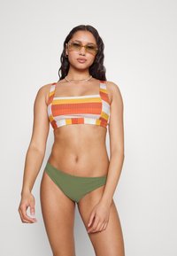 Top de bikini listrado em laranja, amarelo e branco em tecido canelado com decote quadrado; combinado com parte de baixo de bikini em verde-oliva, de textura suave.