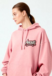 Felpa rosa con tasca frontale, presenta la scritta "Amour" ricamata in bianco e nero, tessuto morbido con una vestibilità rilassata e cappuccio con cordino.