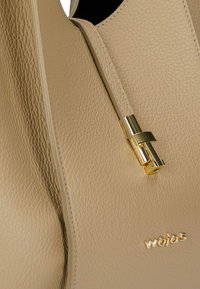 Sac à main en cuir beige texturé avec tirette de fermeture éclair en métal doré et petit logo "wojas" en lettres dorées en bas à droite.