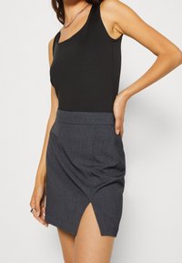 Un haut sans manches noir associé à une mini-jupe grise taillée avec une fente latérale et un tissu texturé, mettant en avant des lignes épurées et un design moderne.