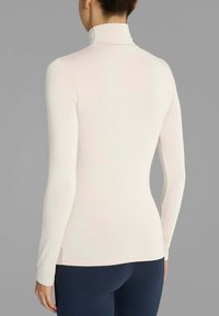 Maglione a maniche lunghe con collo alto in tessuto beige chiaro, texture liscia e design aderente. Fessure laterali all'orlo, abbinato a leggings blu navy.