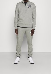 Grau zip-up Sweatshirt mit schwarzem "N"-Logo und passenden grauen Jogginghosen. Features gerippte Bündchen und elastischen Bund, kombiniert mit weißen Sneakers.