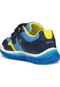 Chaussure bleue et navy avec des panneaux en mesh, accents jaunes, fermeture Velcro et semelle en caoutchouc transparent bleu avec une adhérence texturée.