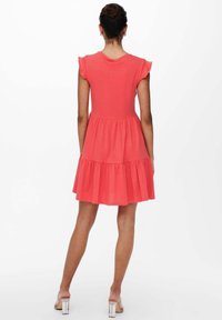 Robe corail à manches courtes avec jupe à volants, encolure arrondie et manches à volant. Confectionnée en tissu doux pour plus de confort.