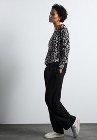Schwarzer und cremefarbener Sweatshirt mit Muster und langen Ärmeln, kombiniert mit lockeren schwarzen Hosen und weißen Turnschuhen. Einfaches Design mit elastischen Bündchen.