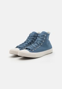 Blue canvas high-top sneakers with white rubber soles and laces, featuring metal eyelets and a textured surface.