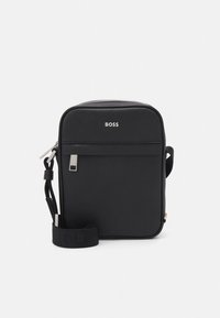 Svart axelremsväska av slätt material, med en framficka med dragkedja, logotypdetaljer och justerbar rem. Rektangulär form.