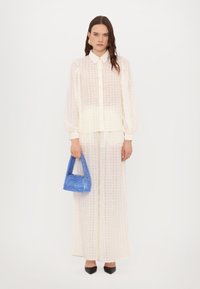 Blusa bianca con texture e motivo a griglia, abbinata a una gonna coordinata e a una borsa blu. Indossata con tacchi a punta neri.