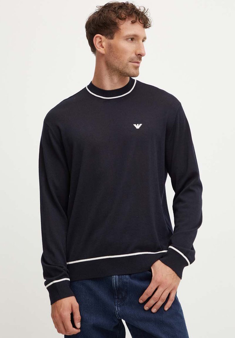 Maglione blu navy con accenti bianchi sul colletto e sull'orlo. Presenta un collo rotondo e un logo ricamato sul petto. Materiale morbido, vestibilità comoda.