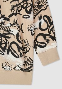 Felpa beige con un design di graffiti in bianco e nero, polsini a costine e tasca frontale. Tessuto morbido con texture variate.