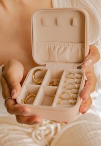 Organisateur de bijoux en tissu doux pêche, comportant des compartiments pour les bagues et une zone rembourrée pour les boucles d'oreilles ; fermeture éclair et texture lisse.