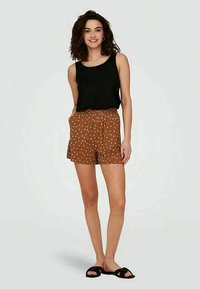 Bruine shorts met een patroon van witte stippen en een zwart tanktop. De shorts hebben een geplooid ontwerp en de outfit is gecombineerd met zwarte sandalen.