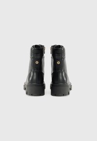 Botas de tobillo de cuero negro con un diseño texturizado, suela de goma gruesa, acentos de hardware dorado y cremallera en la parte posterior para facilitar su uso.