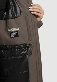 Unutrašnjost jakne s podstavom u smešnoj i crnoj boji, s crnom džepom na vezanje, oznakama brenda i glatkom, sjajnom teksturom.