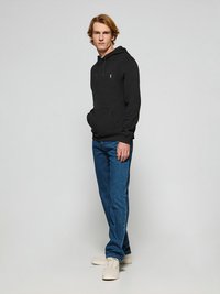 Svart sweatshirt med framficka och dragsko på huvan, tillsammans med blå denimjeans och beige sneakers. Texturerad tyg och avslappnad passform.