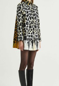 Vestito corto con stampa a giraffa nei colori nero, bianco e ambra; presenta un colletto e maniche lunghe, abbinato a stivali neri al ginocchio.