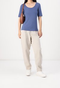 Top azul de manga corta en una tela suave, combinado con pantalones sueltos de color beige claro y zapatillas blancas. Un bolso cruzado marrón añade detalle.