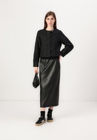 Black textured crop jacket with toggle buttons, paired with a black leather skirt and black sneakers with white stripes. Holding a small black bag.