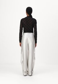 Schwarzes Langarmoberteil mit Karomuster, kombiniert mit glänzenden silbernen weiten Cargo-Hosen, die Taschen und Riemendetails haben.