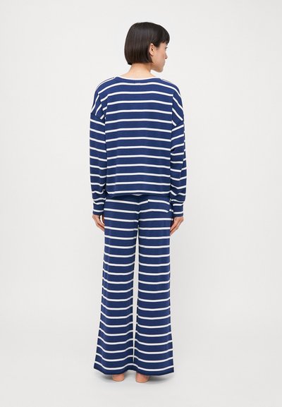 Prugasta loungewear komplet v temno modri in beli barvi, ki vsebuje ohlapen dolg rokav majico in široke hlače, izdelane iz mehke tkanine.