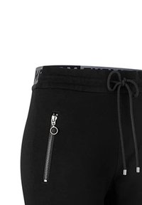 Pantalones de chándal negros con una cintura elástica y cordón. Presentan un bolsillo con cremallera con accesorios plateados. Tejido de textura suave.