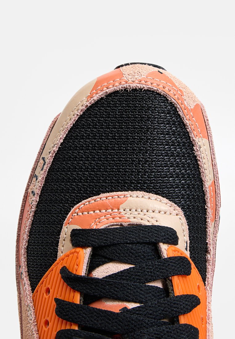 Zapatilla deportiva con parte superior de malla negra, acentos de cuero naranja y beige, suela de goma texturizada y cordones negros con costuras intrincadas.