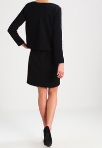 Svart texturerad kortärmad tröja med långa ärmar, kombinerad med en svart knä-lång kjol med en sprund bak, bärs med svarta klackar.