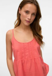 Top sin mangas color coral con un frente texturizado y cintura fruncida. Tejido suave, escote redondeado y tirantes finos.