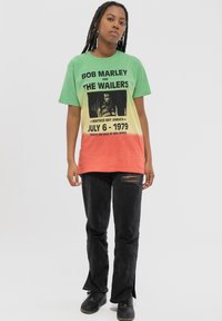 Green to orange gradient T-shirt featuring Bob Marley graphic and text; paired with black distressed jeans and dark footwear.