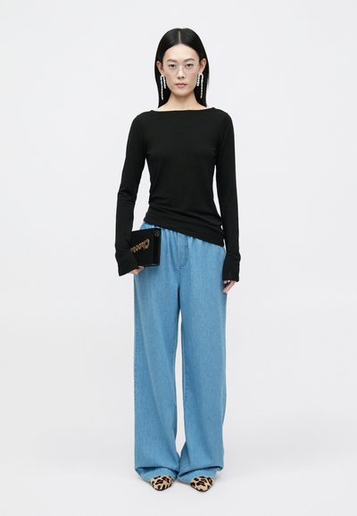 Top preto de manga longa, calças largas de ganga azul relaxadas, sapatos de salto com padrão de leopardo e uma clutch preta com embellishments dourados.