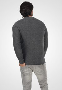 Suéter gris oscuro de tejido de punto texturizado, con mangas largas y escote redondo, combinado con jeans gris claro.