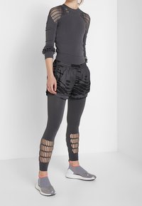 Šedé sportovní tričko s síťovými detaily, v kombinaci s černými šortkami s vzorem a elastickými legínami. Obsahuje nazouvací boty s šedými a oranžovými detaily.