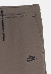 Calças de treino cinzentas com uma textura suave, apresentando um logo preto da Nike, cintura com cordão e bolsos laterais.