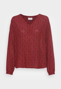 Rote Bluse mit langen Ärmeln und einem schwarzen fächerförmigen geometrischen Muster, V-Ausschnitt und leicht gerafften Bündchen.