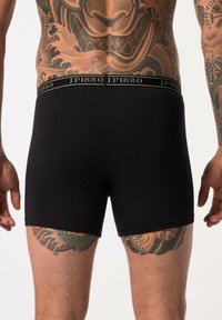 Boxer shorts in cotone nero con una vestibilità aderente e un morbido elastico in vita che presenta il testo "JP1880" in oro. Tatuaggi esposti sulle cosce.