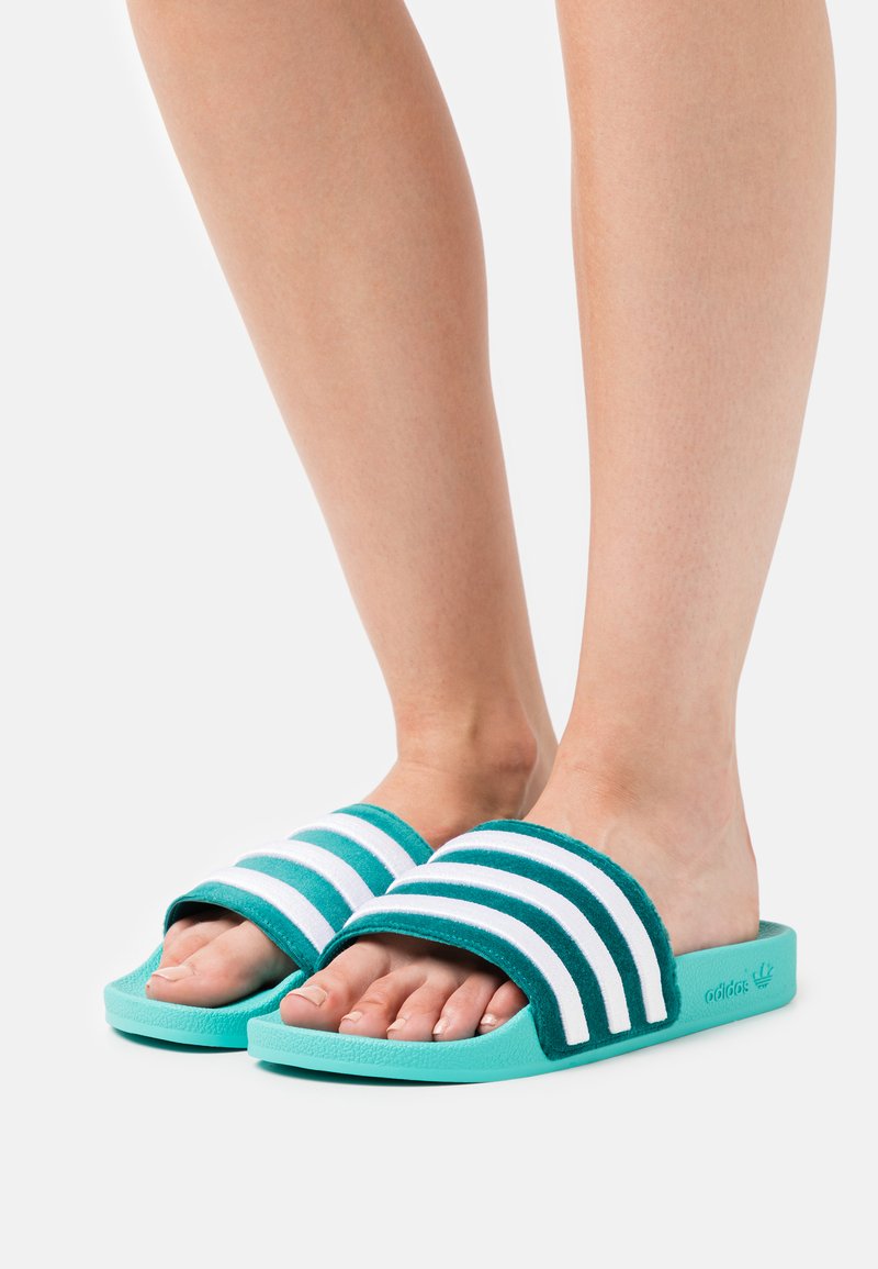 Sandali ciabattine teal con strisce bianche, parte superiore in tessuto morbido e suola in gomma textured. Design open toe che mette in mostra i piedi nudi.