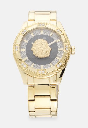 Kuldne kell ümmarguse korpusega ja lõvimoega keskel. Halli taustaga kellaplaat, millel on kristallaktsendid ja tekstureeritud taust. Metallist käevõru kujundus.