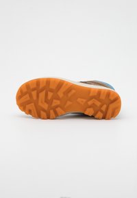 Suela de zapato marrón y azul con una banda de rodadura de goma naranja. Patrones texturizados para un mejor agarre. Entresuela de color claro para mayor comodidad.