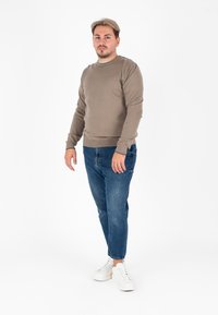 Maglione marrone in un knit testurizzato, abbinato a jeans blu e sneakers bianche. Il maglione presenta un neckline rotondo e polsini a coste.